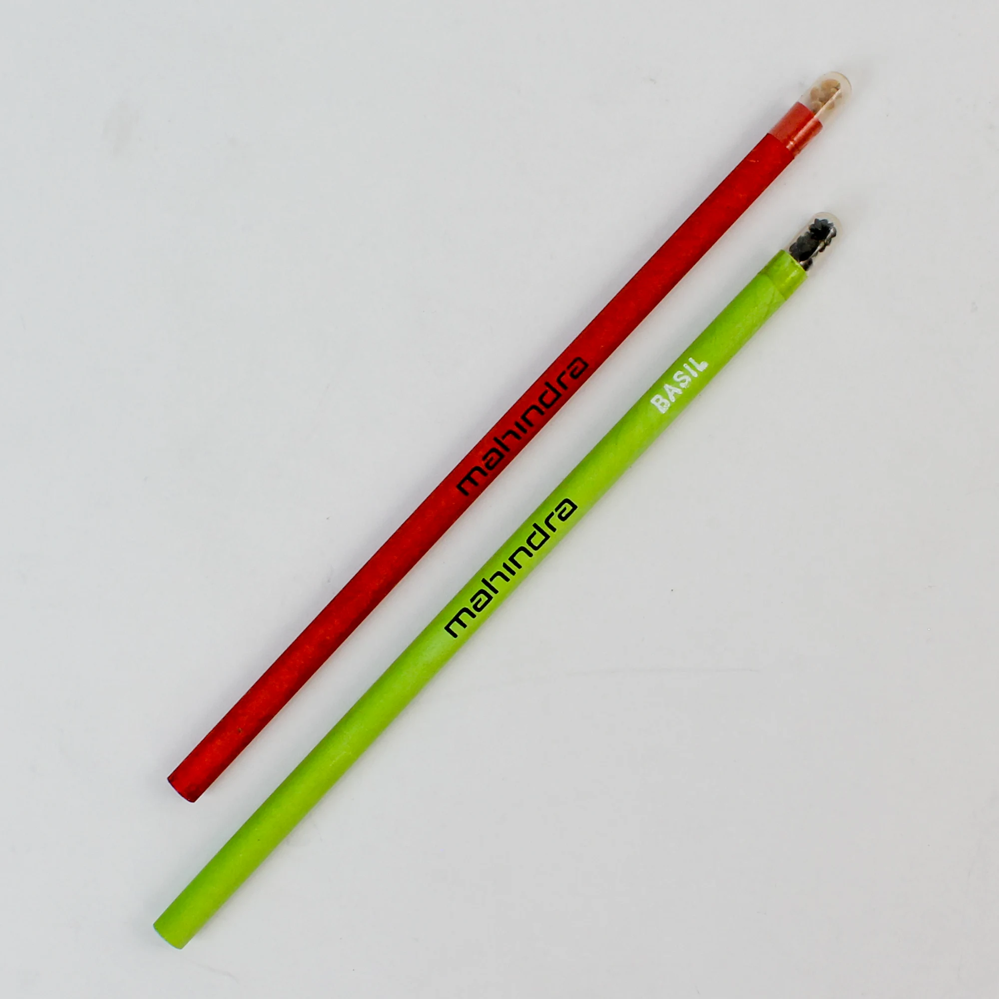 A red and a green seed pencil printed with a corporate logo, the green one also naming basil as its seed