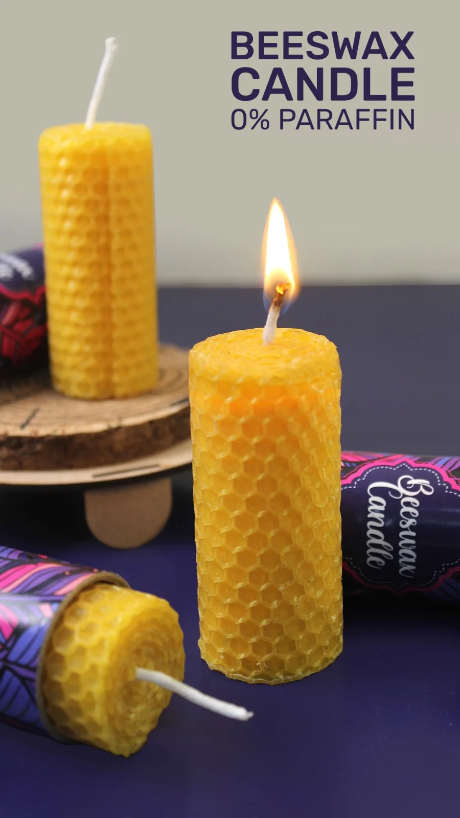 bioQ poster headed beeswax candle, 0% paraffin, showing three honeycomb candles on a dark surface — one lit, one unlit, and one lying in its printed sleeve